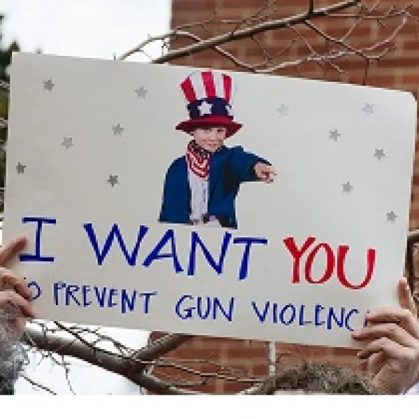 Someone holding up a sign with a picture of a young boy dressed like Uncle Sam and the words I WANT YOU to prevent gun violence