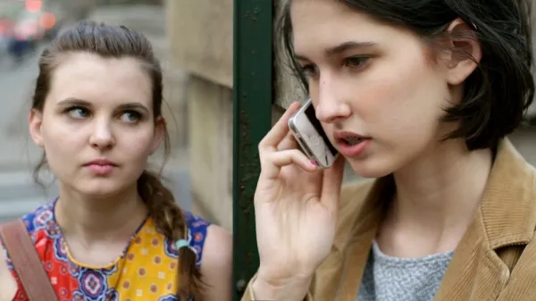 A woman on the phone and another woman looking at her in an alarmed way