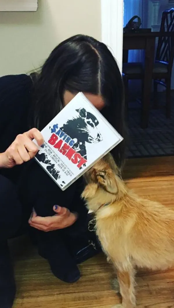 Women with dark hair leaning over hiding her face with a book, Saving Banksy