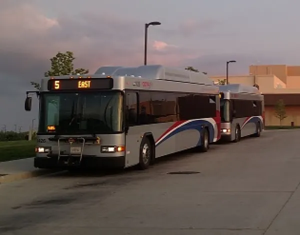 COTA bus, sllver bus with red white and blue curvy stripe on side driving in dusk