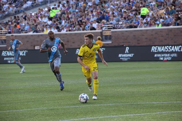 Two soccar players on the field on opposite teams, one in blue and one in yellow kicking the ball