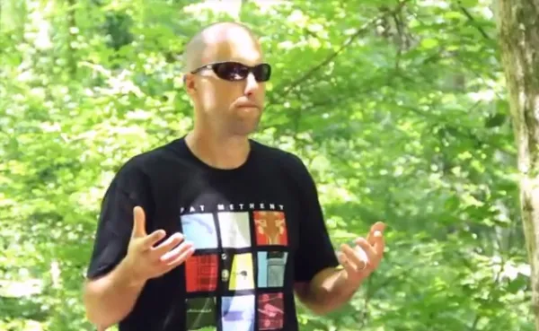 Young white man mostly bald holding his hands out in front of him standing in a forest