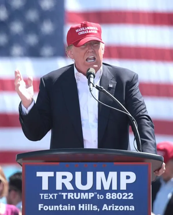 Trump in front of flag with red baseball cap on