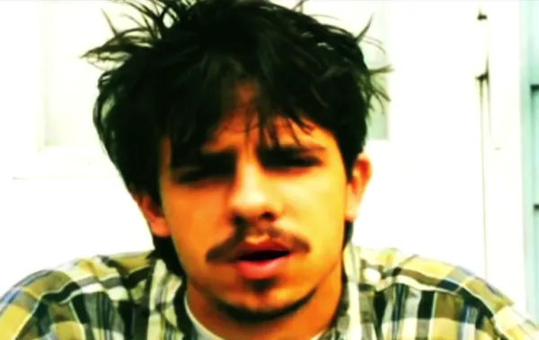 Close up of a young white man's face with dark hair askew and a moustache and goatee