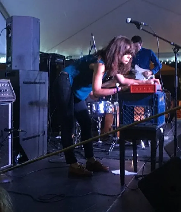 Dark haired woman leaning over a keyboard with a band on a stage