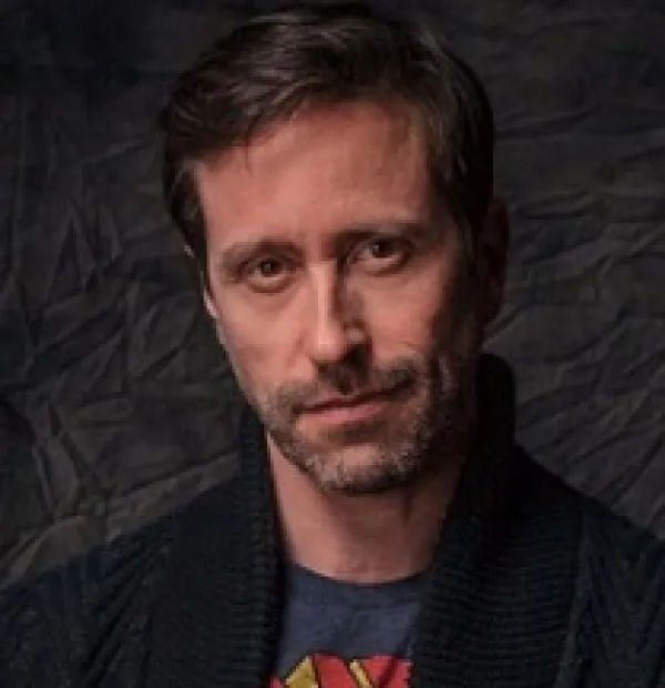 Thin faced man with brown hair and five o clock shadow looking quizzically at the camera