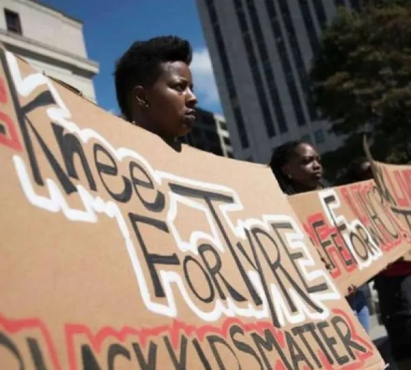 Black people holding a banner that says "Knee for Tyye, Black Kids Matter"