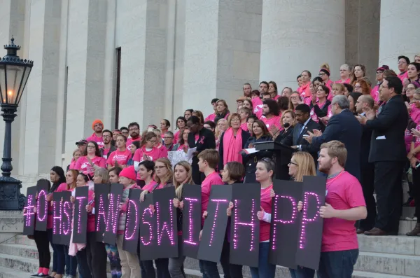 People rallying at the stateouse wearing pink shirts