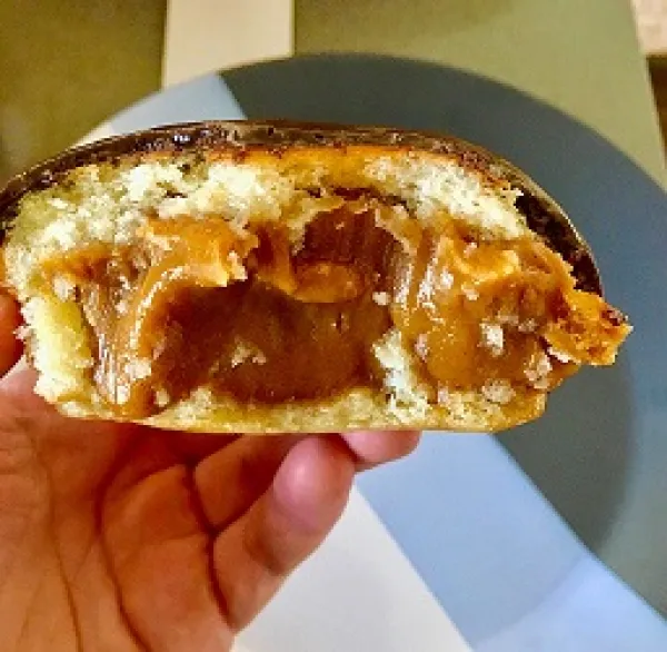 A hand holding a pastry that seems to be filled with yellowish fruit