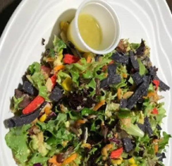 Salad on a plate with a little cup of salad dressing at the side