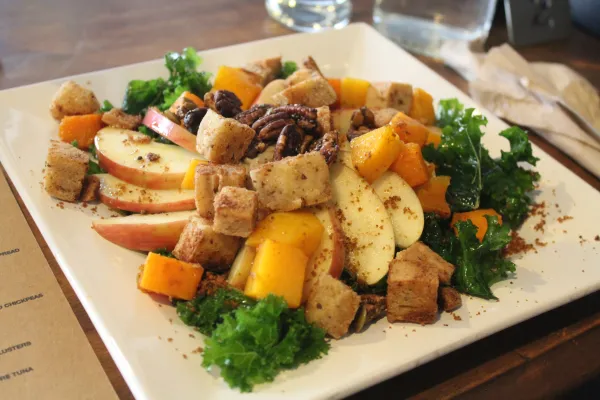 A square white plate filled with vegetables and green garnishes