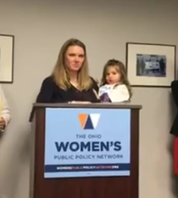 Woman holding a baby at a podium that says Women's Public Policy Network