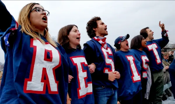 People dressed in red, white and blue with RESIST spelled out on each shirt yelliing