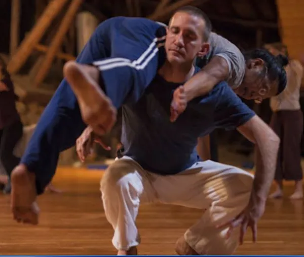 White middle aged man squatting with his eyes closed holding a woman across is back in a dance move